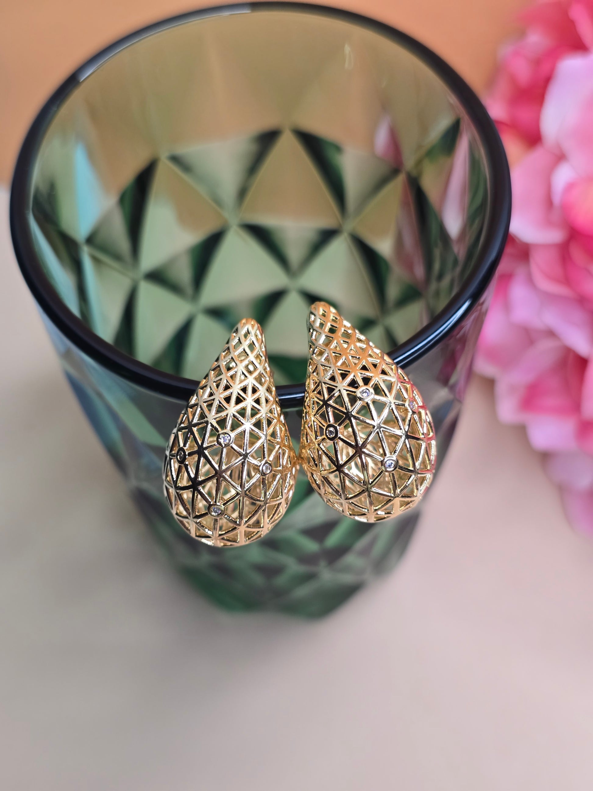 A pair of 18k gold-plated, Bottega-inspired earrings with a geometric pattern and circle zircons, displayed against a faceted glass container. The earrings are available in two sizes, Small (SM) and Large (L).